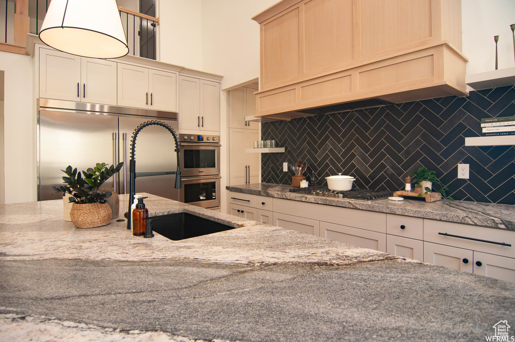 Kitchen featuring sink, light stone counters, tasteful backsplash, and appliances with stainless steel finishes