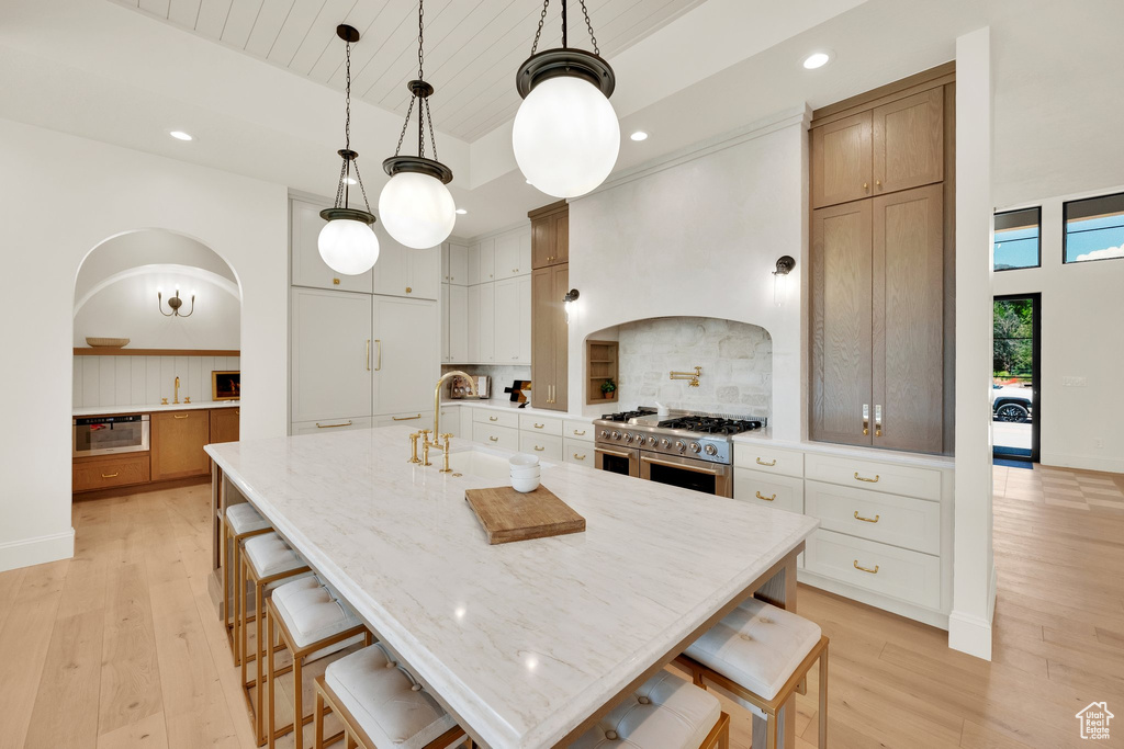 Kitchen with appliances with stainless steel finishes, light wood finished floors, tasteful backsplash, a breakfast bar area, and recessed lighting