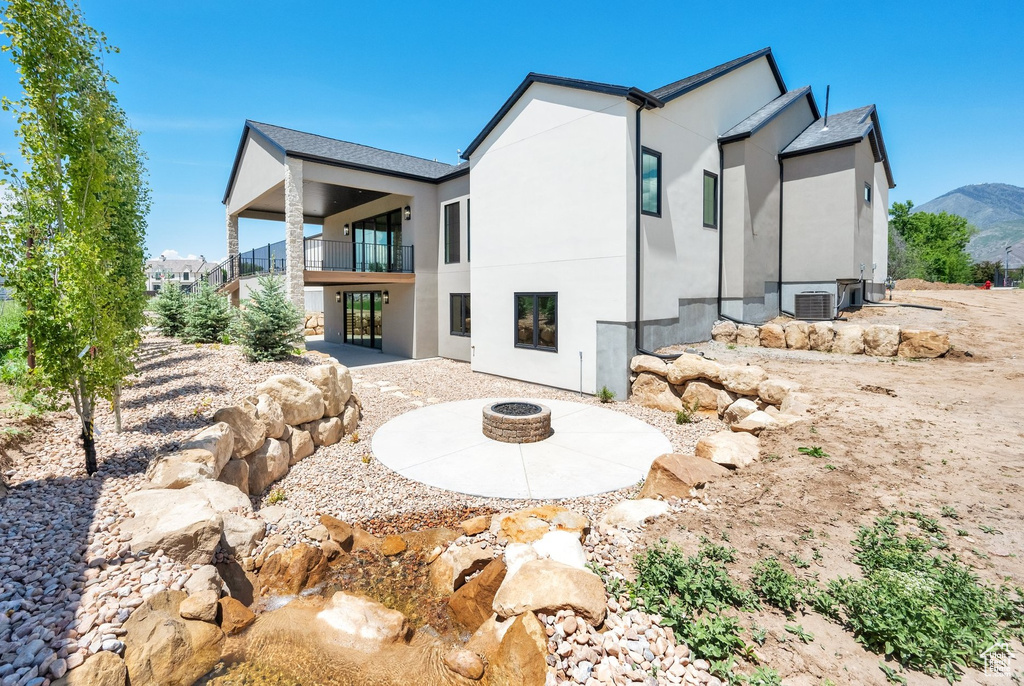 Rear view of house featuring a fire pit, a balcony, stucco siding, a patio, and central AC unit