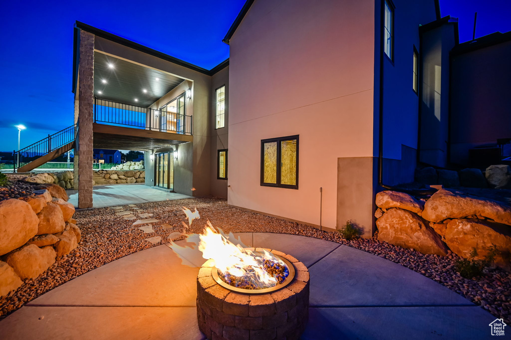 Back of house at twilight featuring an outdoor fire pit, a patio, stairs, a balcony, and stucco siding