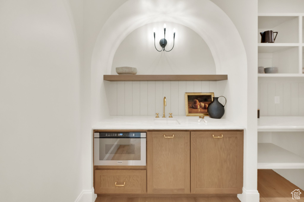 Indoor wet bar featuring stainless steel oven, built in shelves, and light wood-type flooring