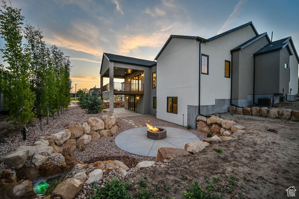 Rear view of house with an outdoor fire pit, a patio, cooling unit, a balcony, and stucco siding