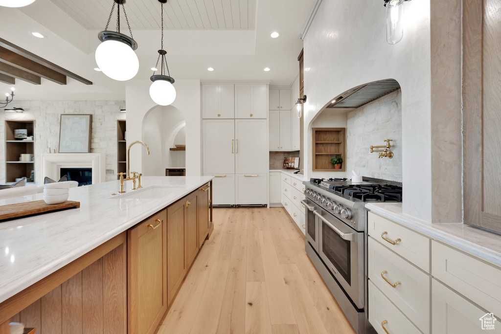 Kitchen with range with two ovens, a sink, light wood-style flooring, white cabinetry, and recessed lighting