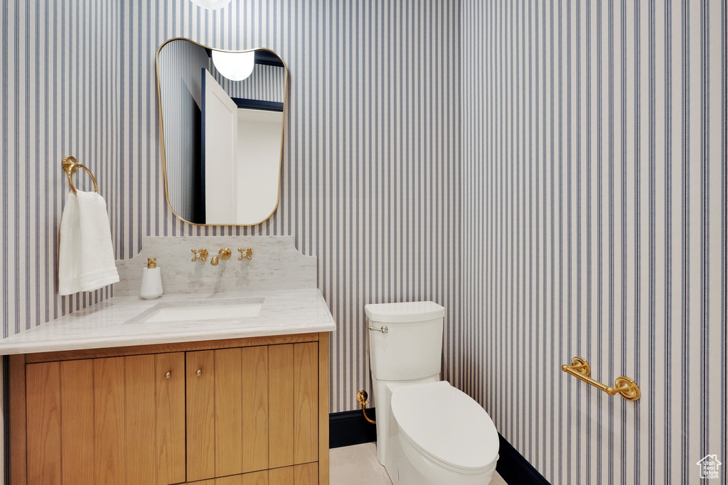 Half bathroom with wallpapered walls, vanity, and toilet