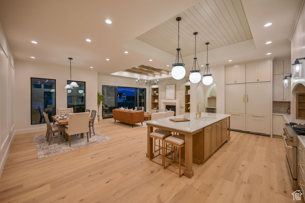Kitchen with a tray ceiling, light wood-type flooring, a sink, high end stove, and a spacious island