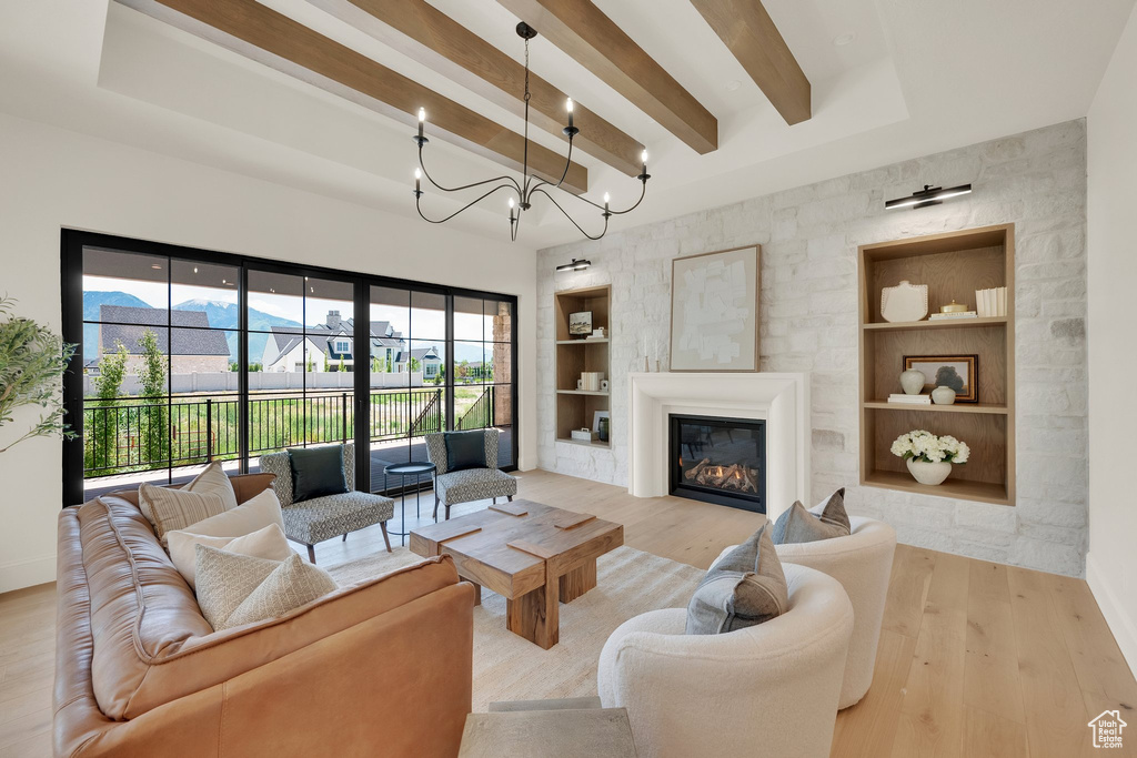 Living area featuring built in features, beam ceiling, wood finished floors, baseboards, and a glass covered fireplace