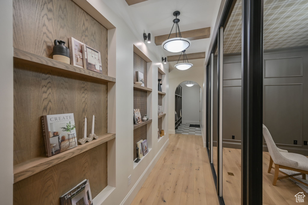 Corridor with arched walkways, built in features, light wood-type flooring, and baseboards