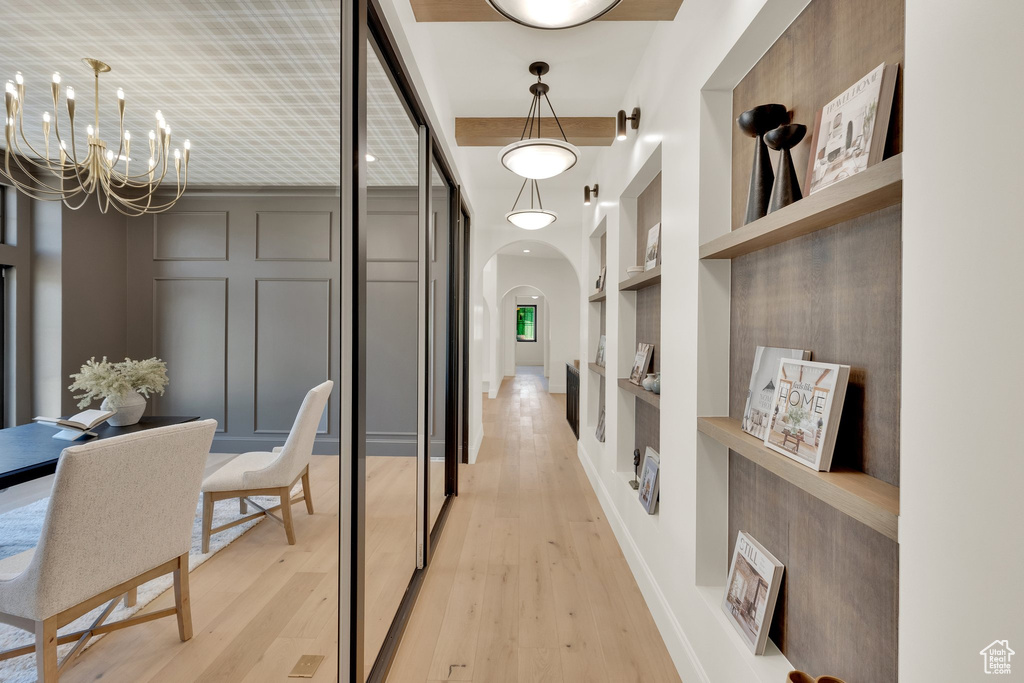 Hallway featuring built in features, arched walkways, a chandelier, and light wood-style floors