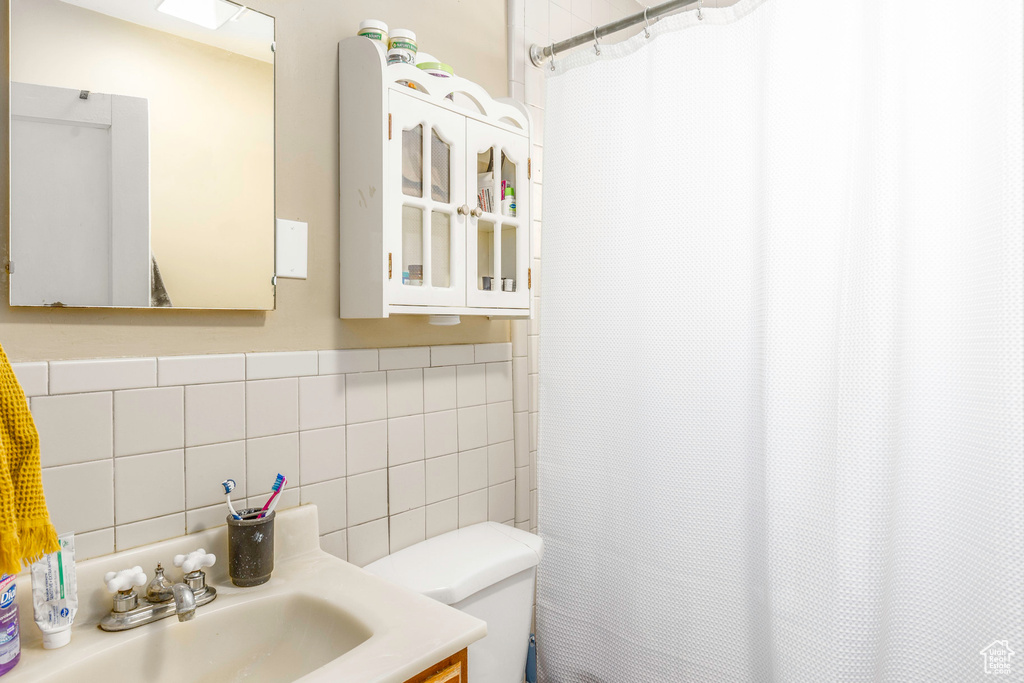 Bathroom with backsplash, vanity, toilet, and tile walls