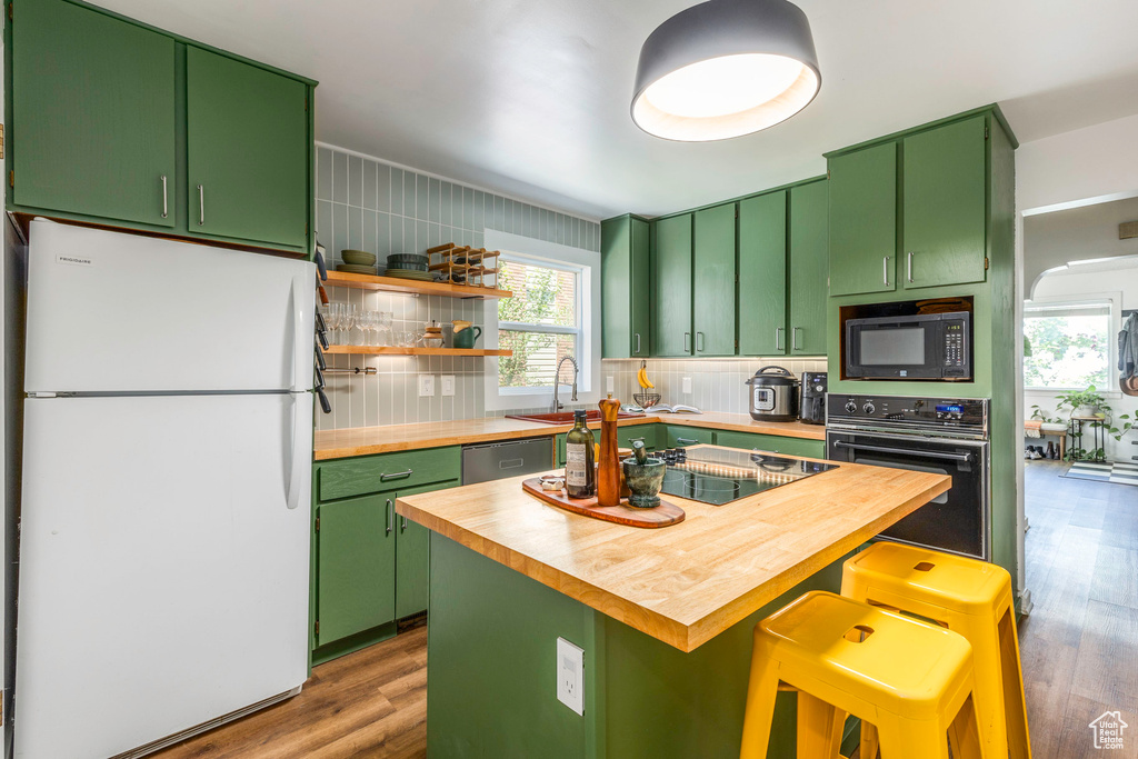 Kitchen featuring green cabinetry, black appliances, tasteful backsplash, and wood counters