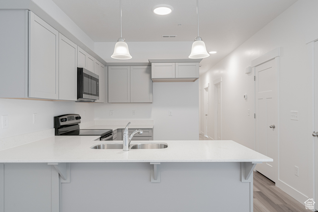 Kitchen featuring appliances with stainless steel finishes, sink, light hardwood / wood-style floors, hanging light fixtures, and a breakfast bar area