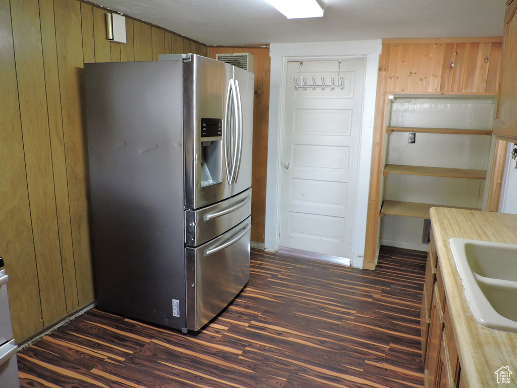 Kitchen with sink, dark hardwood / wood-style floors, stainless steel refrigerator with ice dispenser, and wood walls