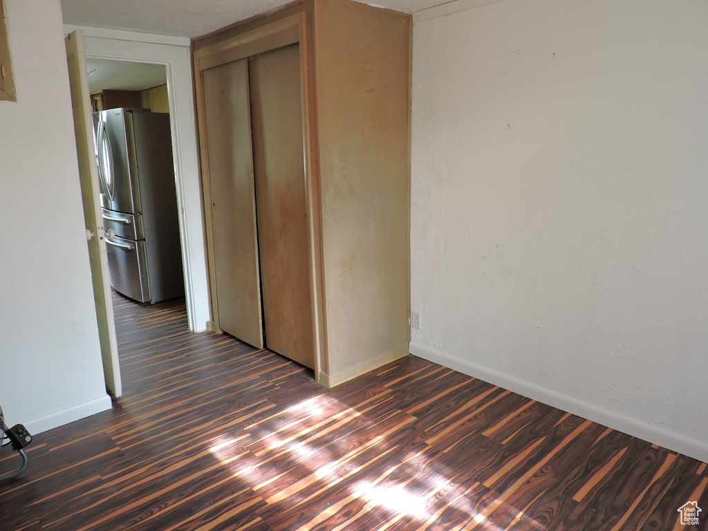 Unfurnished bedroom featuring a closet, stainless steel refrigerator, and dark wood-type flooring