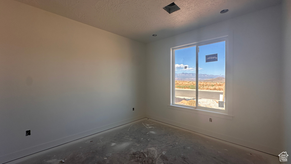 Empty room featuring a mountain view, a textured ceiling, and concrete flooring