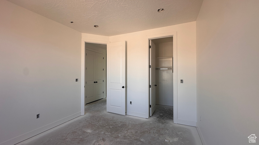 Unfurnished bedroom with a closet, a textured ceiling, a walk in closet, and concrete flooring