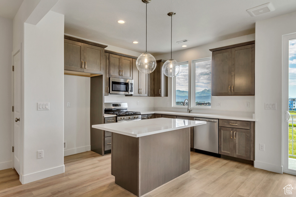 Kitchen with stainless steel appliances, a kitchen island, light hardwood / wood-style flooring, and a healthy amount of sunlight