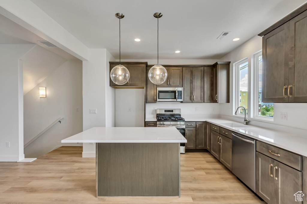 Kitchen with a center island, light wood-type flooring, stainless steel appliances, decorative light fixtures, and sink