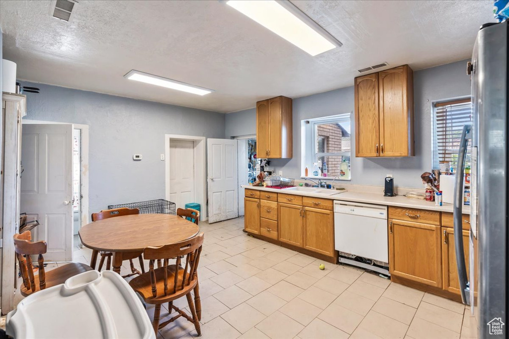 Kitchen featuring stainless steel refrigerator, light tile flooring, white dishwasher, sink, and a textured ceiling