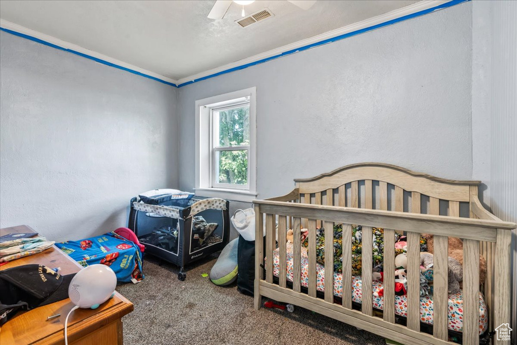 Carpeted bedroom with ceiling fan, crown molding, and a nursery area