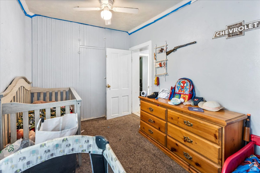 Bedroom with a crib, dark colored carpet, crown molding, and ceiling fan