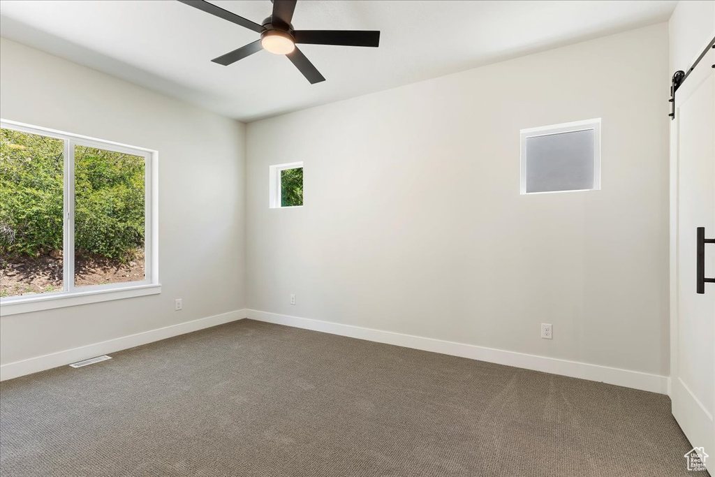 Carpeted empty room featuring a barn door and ceiling fan