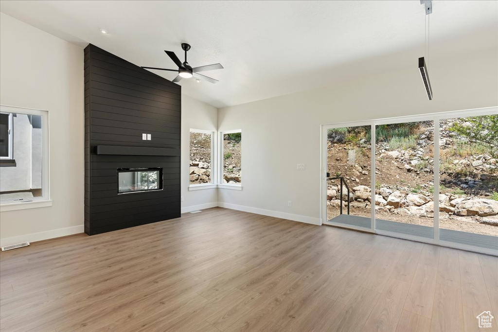 Unfurnished living room featuring ceiling fan, light hardwood / wood-style flooring, a fireplace, high vaulted ceiling, and wood walls