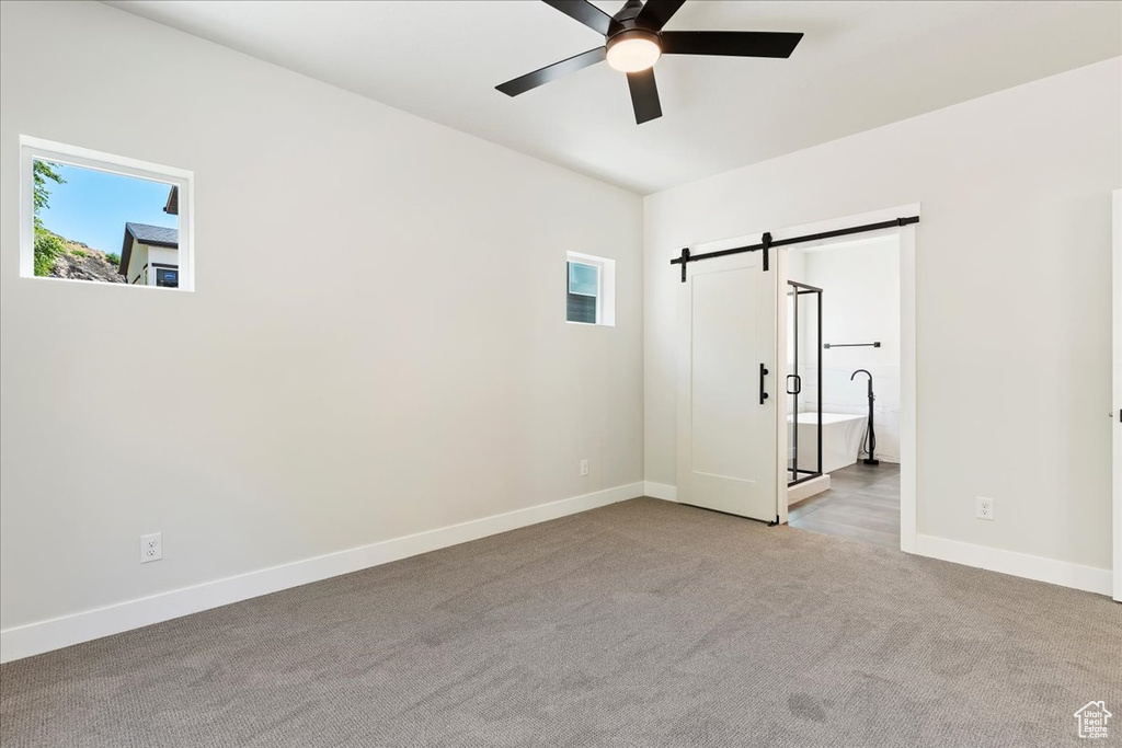 Unfurnished bedroom featuring connected bathroom, carpet, a barn door, and ceiling fan