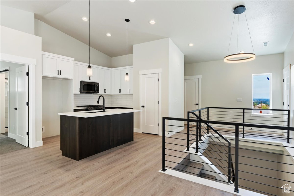 Kitchen featuring tasteful backsplash, a kitchen island with sink, light wood-type flooring, lofted ceiling, and white cabinetry