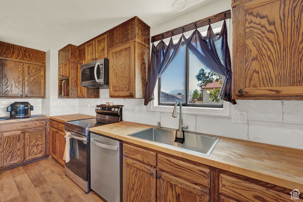 Kitchen featuring light hardwood / wood-style floors, backsplash, butcher block countertops, appliances with stainless steel finishes, and sink