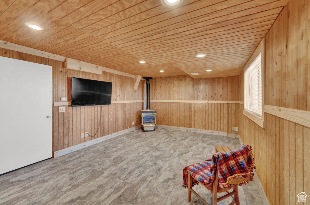 Unfurnished room with wood ceiling, wood walls, and a wood stove