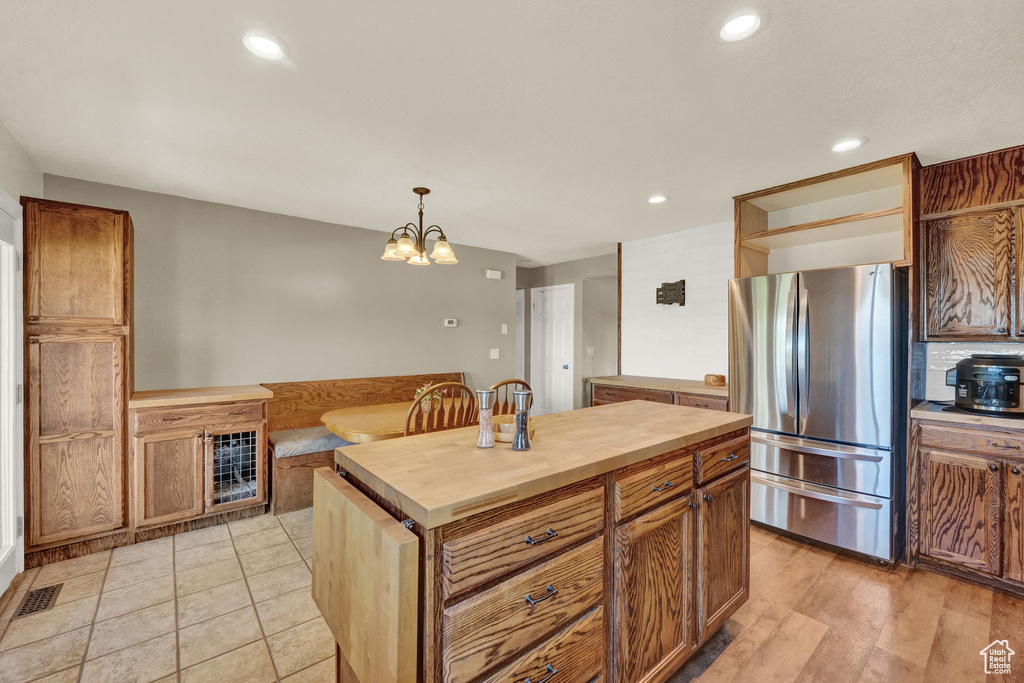 Kitchen with hanging light fixtures, a kitchen island, light hardwood / wood-style flooring, wooden counters, and stainless steel refrigerator