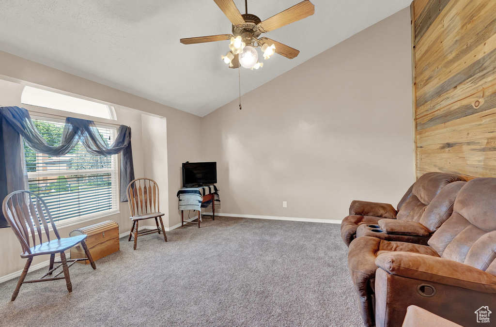 Living area featuring wooden walls, ceiling fan, carpet flooring, and high vaulted ceiling