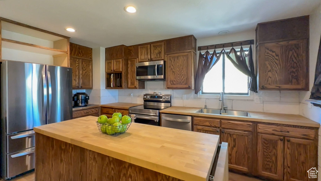 Kitchen featuring butcher block countertops, backsplash, a center island, sink, and appliances with stainless steel finishes