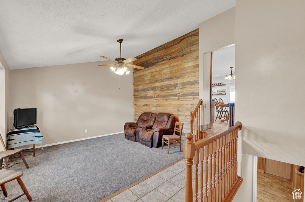 Sitting room featuring wooden walls, tile floors, ceiling fan with notable chandelier, and lofted ceiling