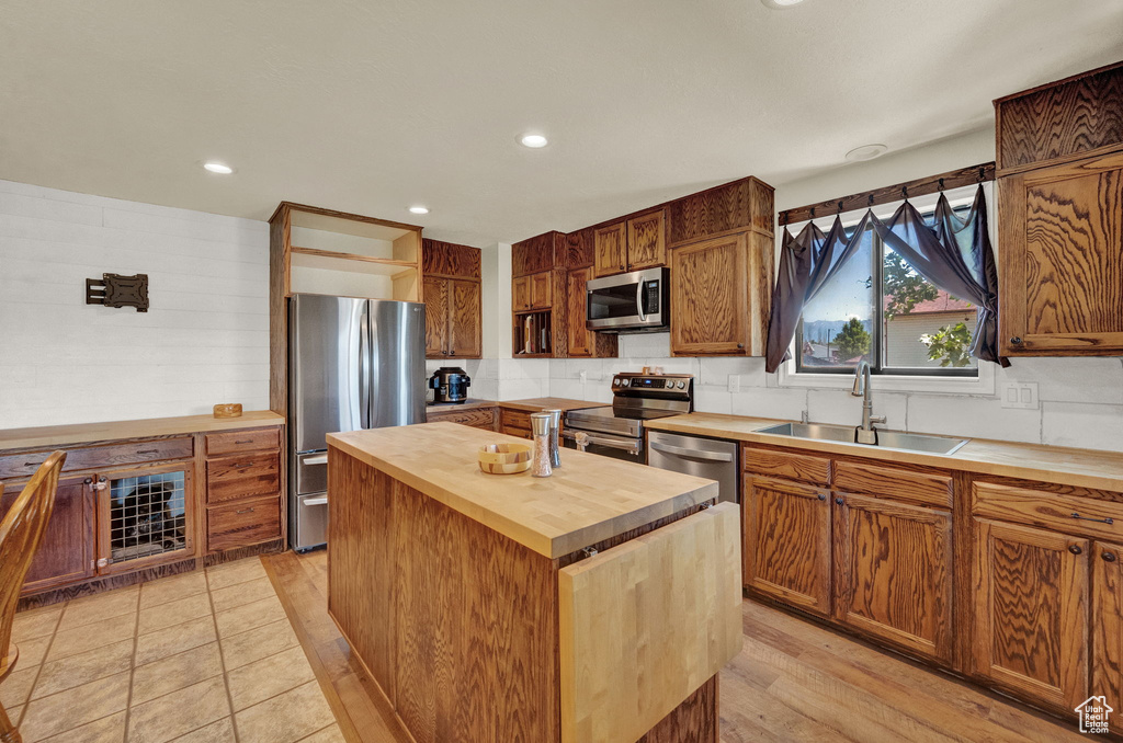 Kitchen with a center island, light hardwood / wood-style flooring, appliances with stainless steel finishes, butcher block countertops, and sink