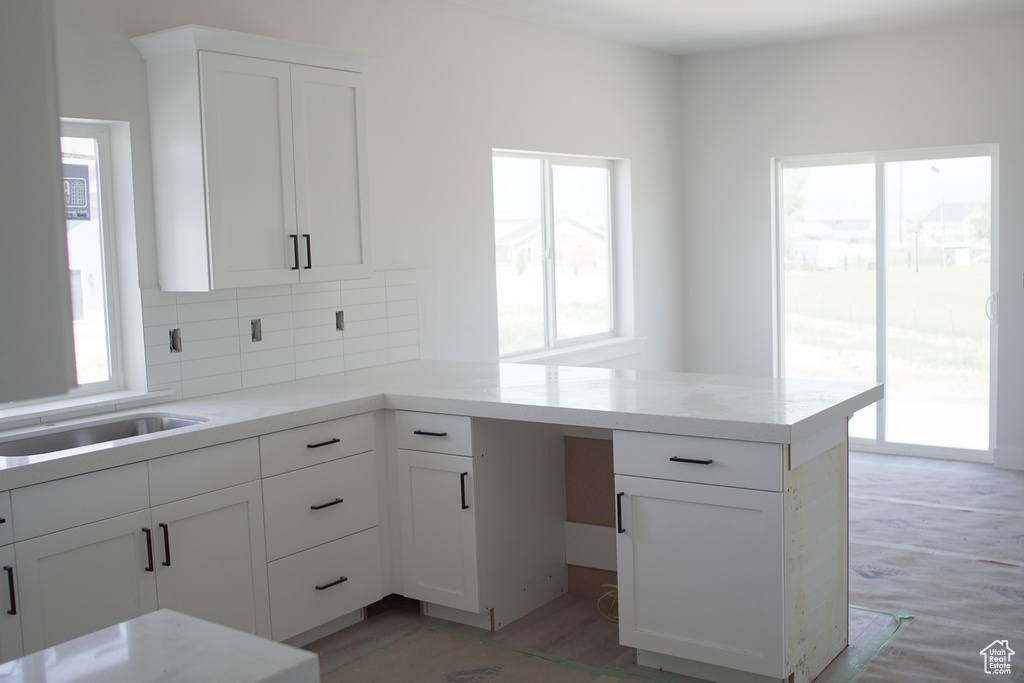 Kitchen with a peninsula, healthy amount of natural light, white cabinets, and backsplash