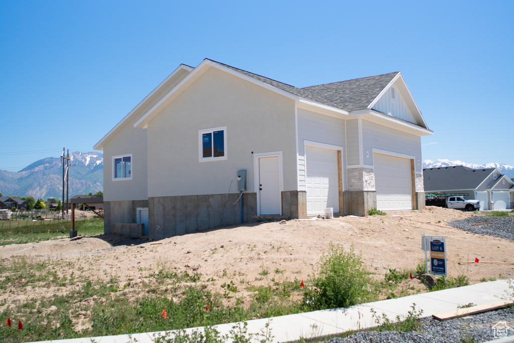 View of side of home featuring a garage, a mountain view, a shingled roof, and driveway