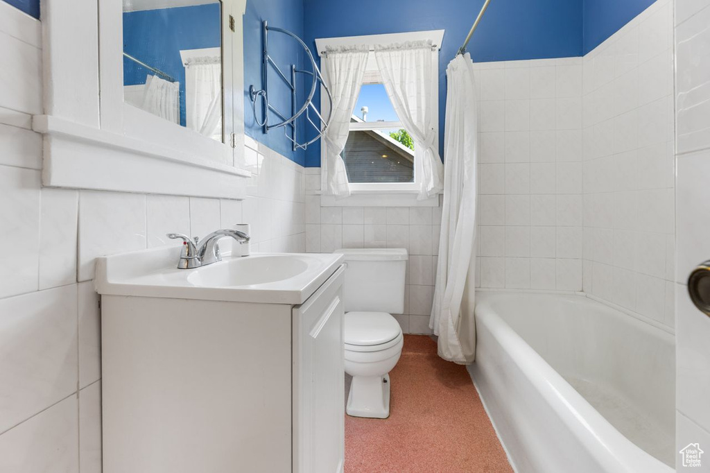 Full bathroom with large vanity, tile walls, toilet, and shower / tub combo with curtain