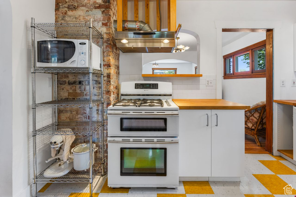 Kitchen featuring white appliances, butcher block countertops, light tile flooring, backsplash, and white cabinetry