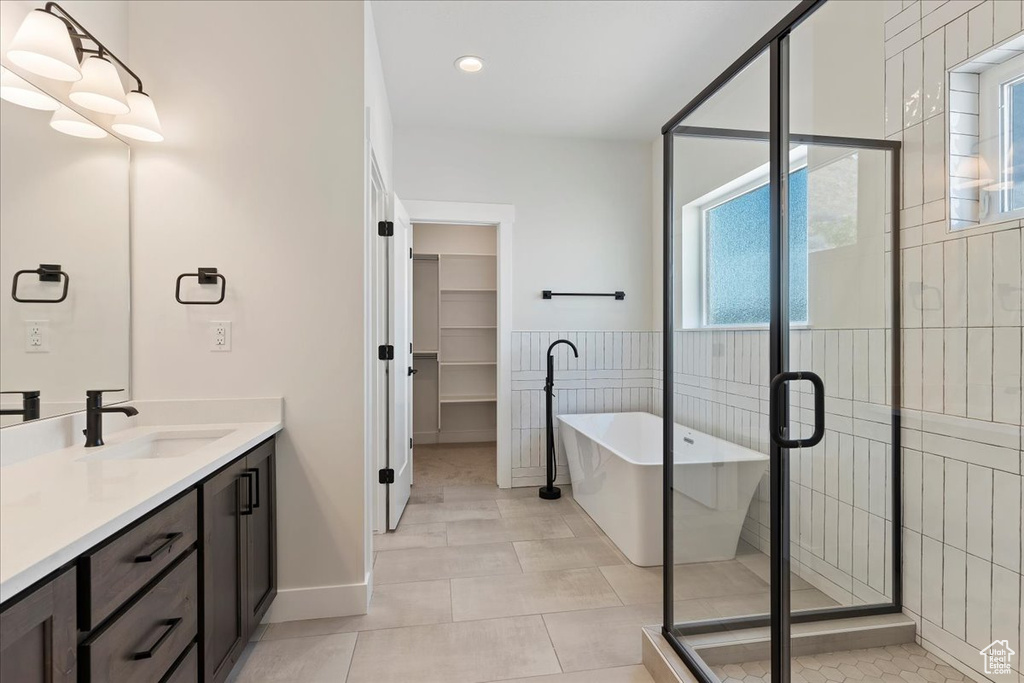 Bathroom with tile floors, tile walls, separate shower and tub, and vanity