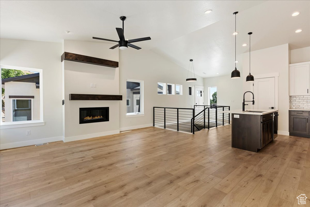 Unfurnished living room featuring high vaulted ceiling, sink, ceiling fan, and light hardwood / wood-style flooring