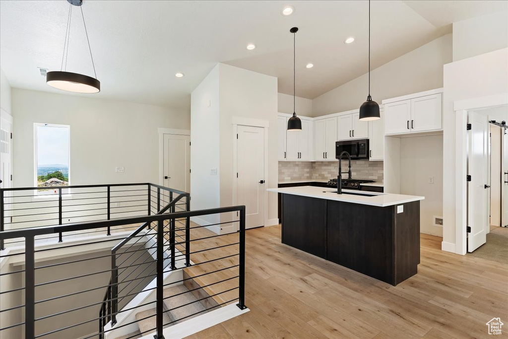 Kitchen featuring white cabinets, backsplash, vaulted ceiling, and light hardwood / wood-style flooring