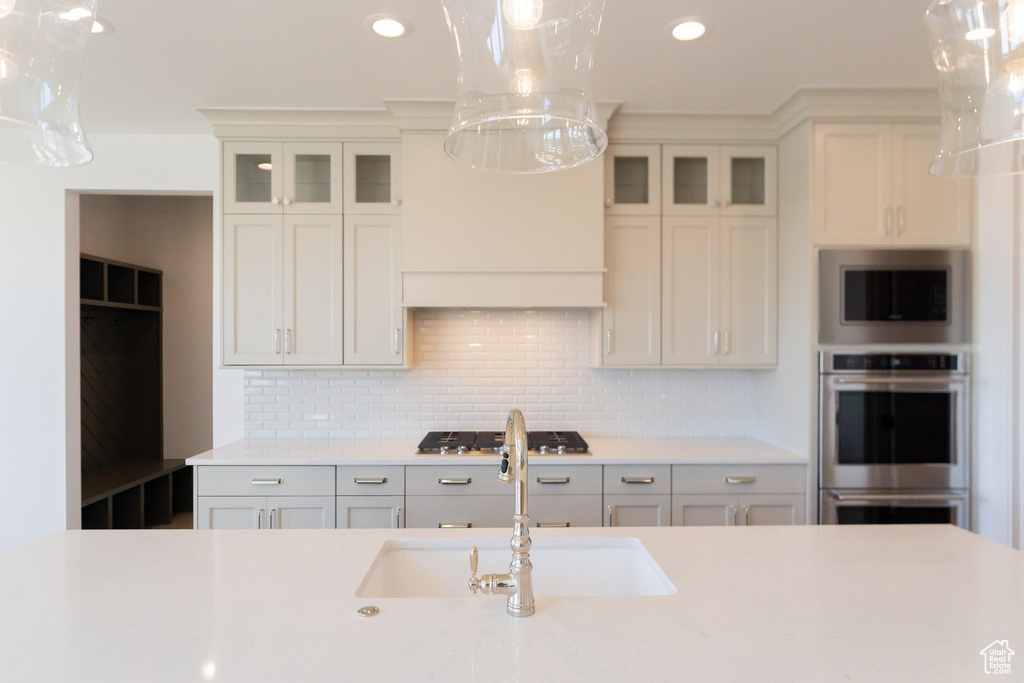 Kitchen with decorative light fixtures, gas cooktop, tasteful backsplash, sink, and stainless steel double oven