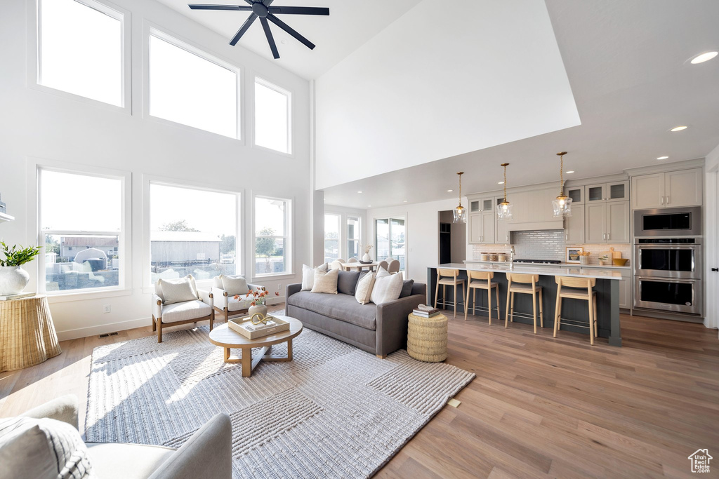 Living room featuring a towering ceiling, light hardwood / wood-style flooring, and ceiling fan