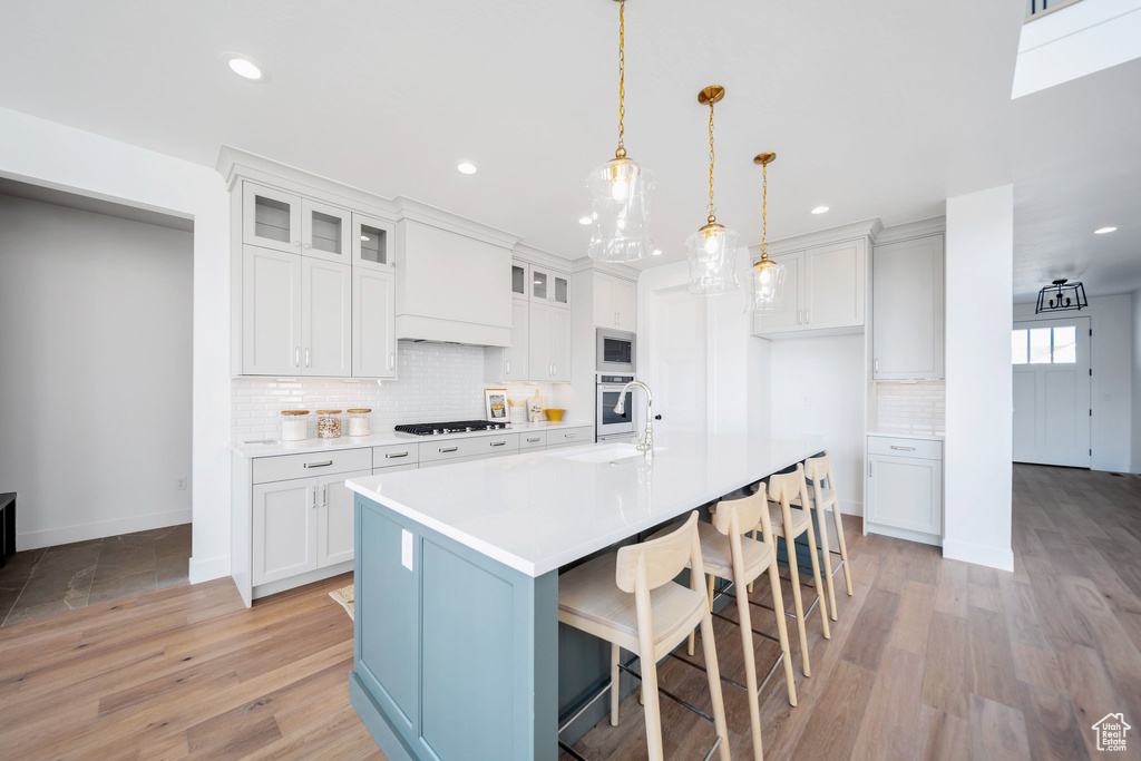 Kitchen featuring light hardwood / wood-style floors, decorative light fixtures, decorative backsplash, and a kitchen island with sink