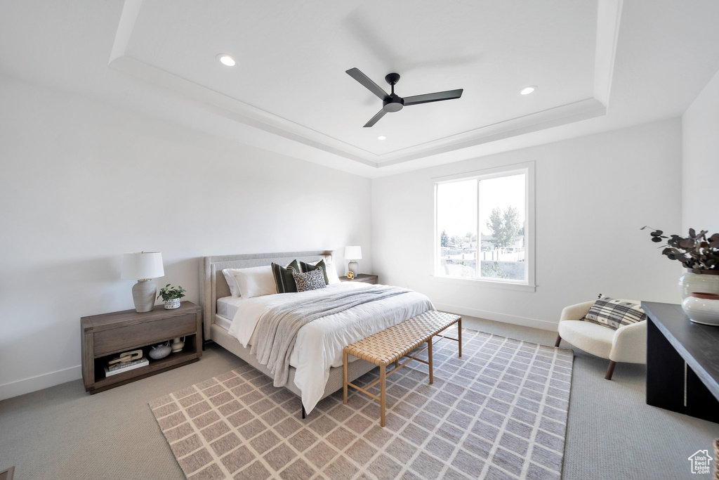 Carpeted bedroom featuring ceiling fan and a tray ceiling