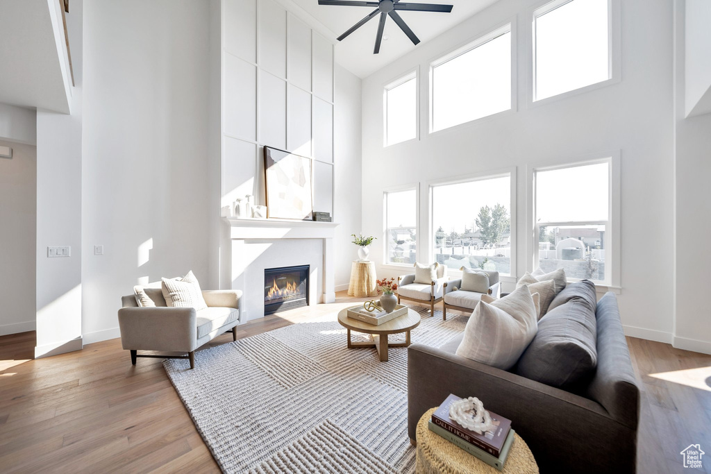 Living room with a large fireplace, light hardwood / wood-style flooring, ceiling fan, and a high ceiling