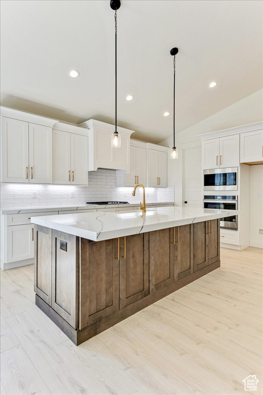 Kitchen with hanging light fixtures, a spacious island, light wood-type flooring, stainless steel appliances, and backsplash