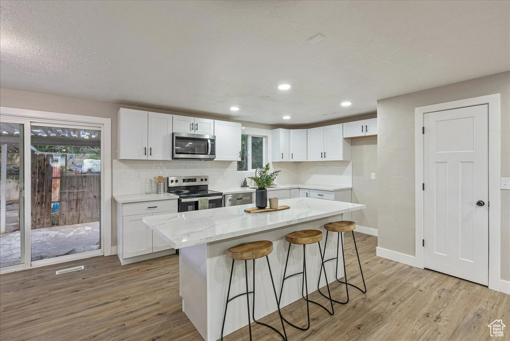 Kitchen with light hardwood / wood-style floors, a kitchen island, stainless steel appliances, white cabinetry, and a breakfast bar