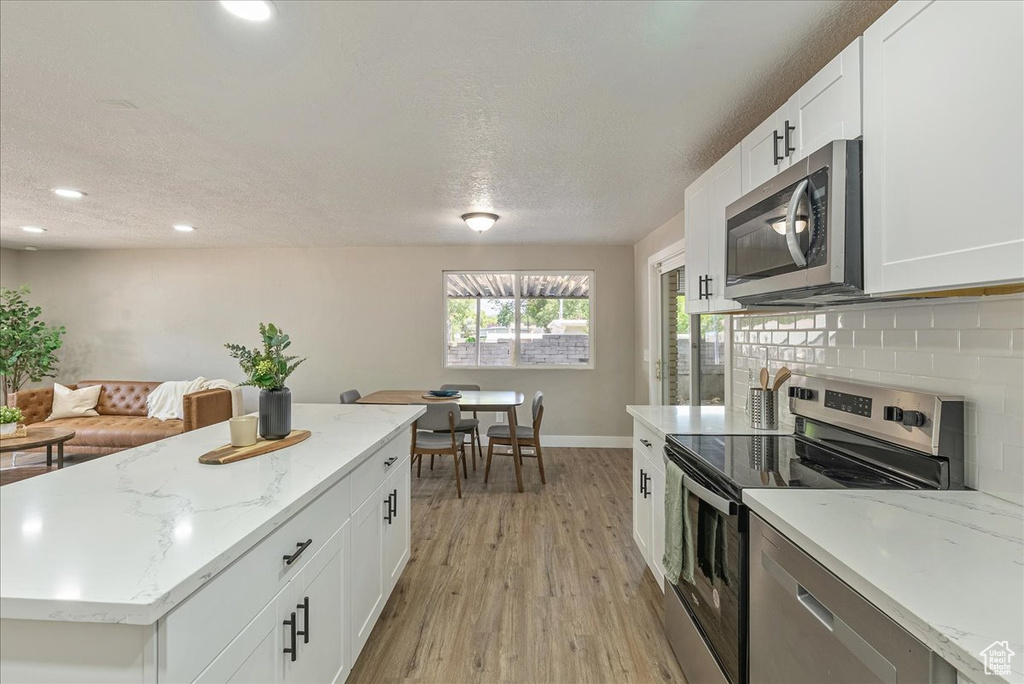 Kitchen with light stone countertops, light hardwood / wood-style flooring, tasteful backsplash, stainless steel appliances, and white cabinets